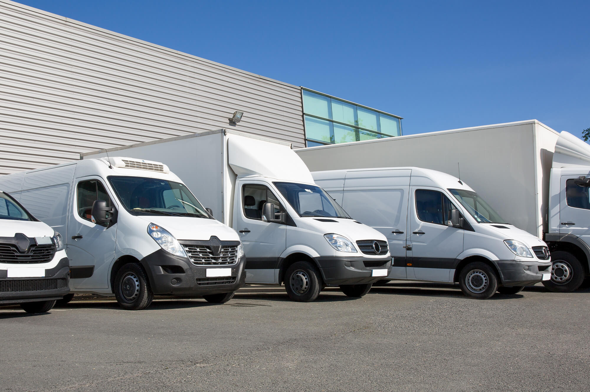 Fünf weiße Fahrzeuge, die in Reihe geparkt sind. Vom PKW über Kleintransporter bis zum LKW, eine kleine Flotte unterschiedlicher Firmenfahrzeuge.