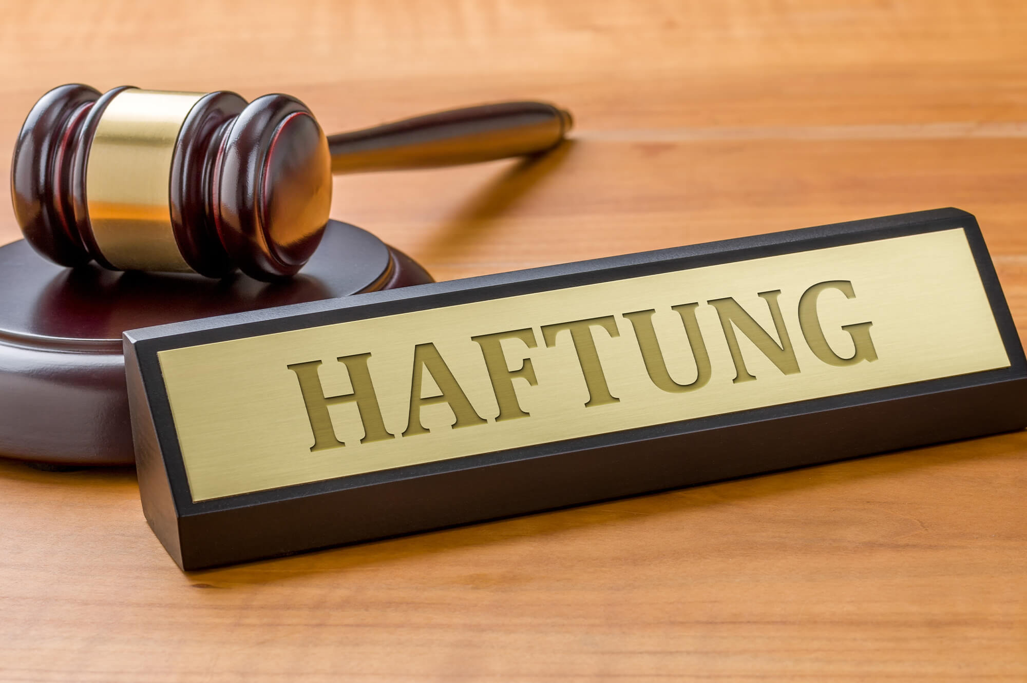 Man sieht eine Tischoberfläche, darauf befindet sich ein Schild mit dem Wort „Haftung“ und ein Richterhammer.